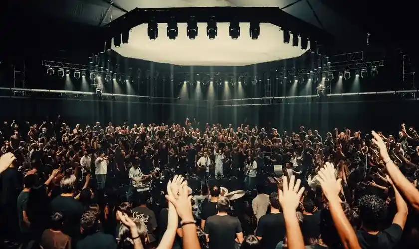 Igreja reunida em louvor, com as mãos levantadas diante da banda no palco